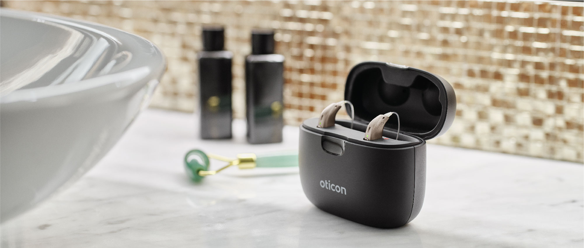 Zwei Oticon Akku-Hörsysteme im offenen Ladeetui auf Marmoroberfläche mit Kosmetikflaschen und Gesichtsmassagegerät​​​​​​​​​​​​​​​​​​​​​​​​​​​​​​​