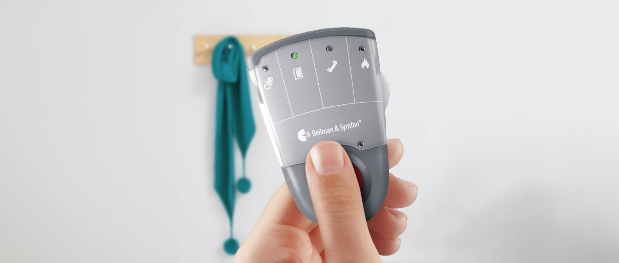 Nahaufnahme eines Bellman & Symfon Pagers in Hand vor weißer Wand mit Haken und grünem Schal​​​​​​​​​​​​​​​​​​​​​​​​​​​​​​​​​​​​​​​​​​​​​​​​​​​​​