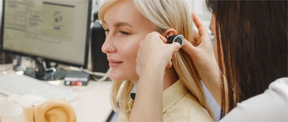 HNO-Arzt passt einer Frau in der Praxis ein Hörgerät an. Moderne Hörgeräte und medizinische Untersuchung sind sichtbar.​​​​​​​​​​​​​​​​​​​​​​​​​​