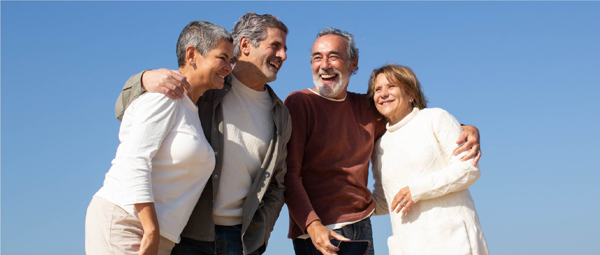 Vier Erwachsene umarmen sich lachend unter klarem Himmel, symbolisieren Gemeinschaft und Bewusstsein stärken im Freien.​​​​​​​​​​​​​​​​​​​​​​​​​​