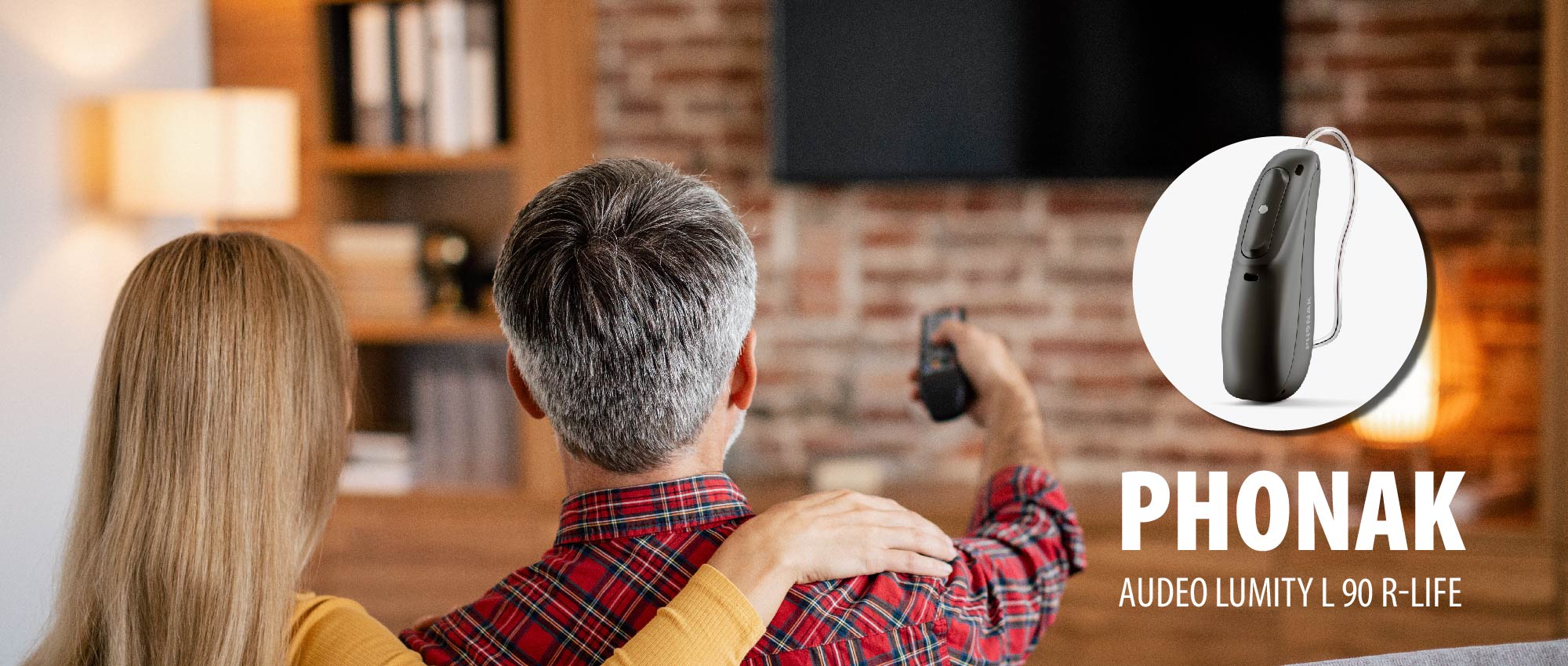 Paar sitzt auf Sofa vor Fernseher mit Fernbedienung, Bluetooth Hörgerät Phonak Audeo Lumity sichtbar​​​​​​​​​​​​​​​​​​​​​​​​​​​​​​​​​​​​​​​​​​​​​