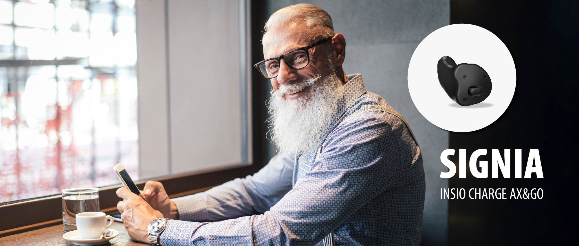 Älterer Mann mit Bart und Brille nutzt Smartphone im Café, zeigt modernes Bluetooth Hörgerät für bessere Hörqualität.​​​​​​​​​​​​​​​​​​​​​​​​​​​​