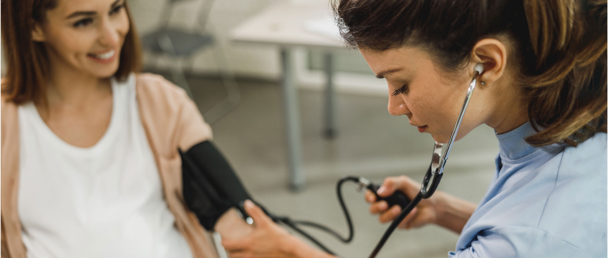 Medizinische Fachkraft misst Blutdruck einer lächelnden Frau in heller Praxis mit Stethoskop und Manschette​​​​​​​​​​​​​​​​​​​​​​​​​​​​​​​​​​​​​​