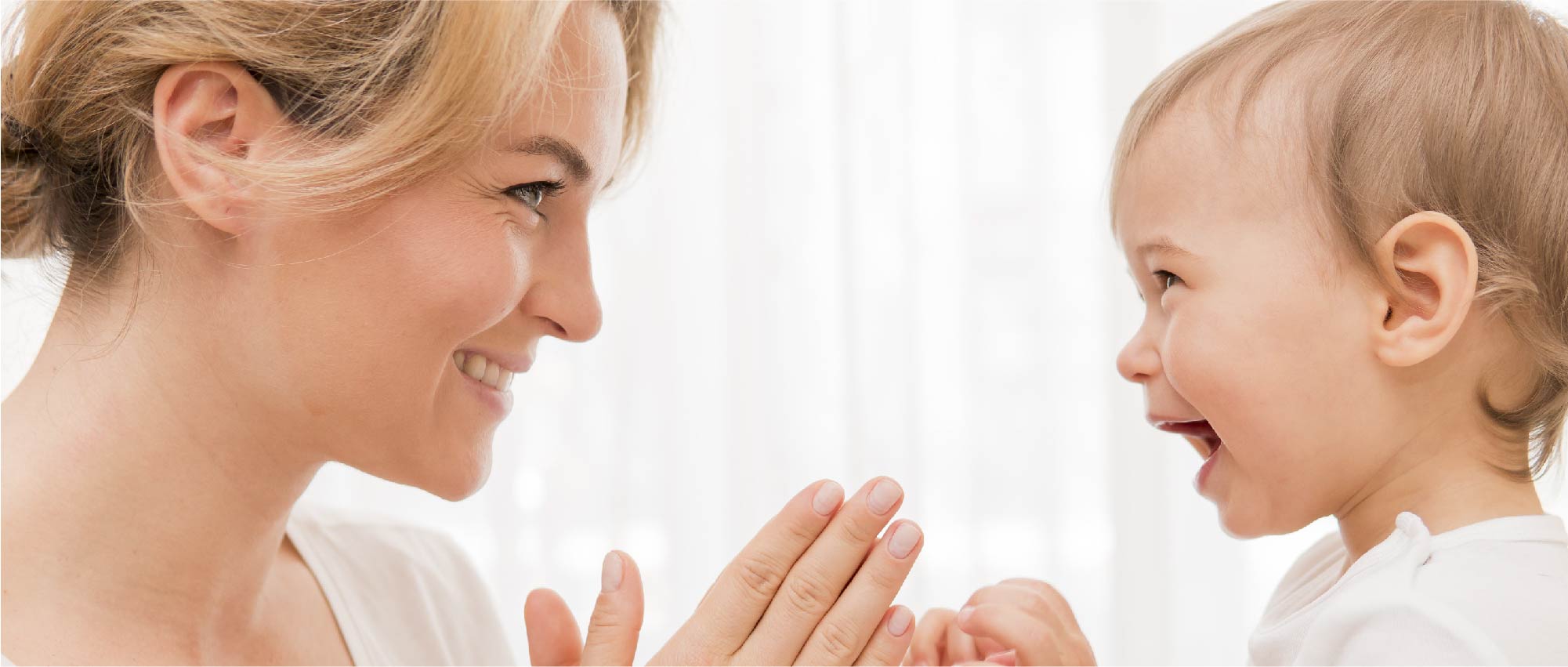 Mutter und Kleinkind spielen fröhlich mit Händen vor hellem Hintergrund in der frühkindlichen Versorgung​​​​​​​​​​​​​​​​​​​​​​​​​​​​​​​​​​​​​​​​​