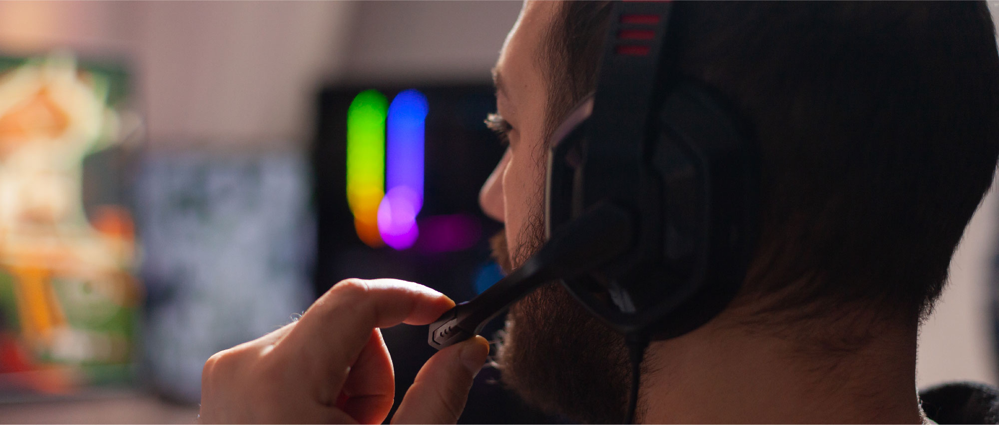 Nahaufnahme eines Mannes mit Gaming-Headset, der das Mikrofon einstellt, vor einem PC mit bunter RGB-Beleuchtung​​​​​​​​​​​​​​​​​​​​​​​​​​​​​​​​​