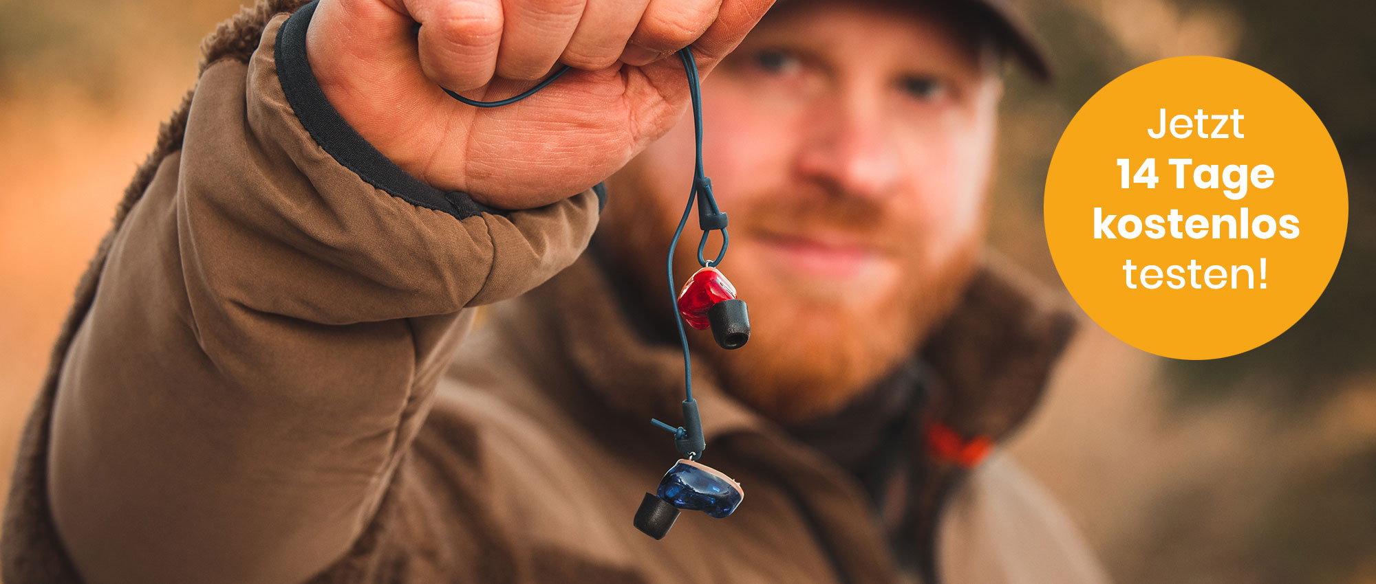 Nahaufnahme eines Jägers mit brauner Jacke, der roten und blauen Gehörschutz im Wald zeigt​​​​​​​​​​​​​​​​​​​​​​​​​​​​​​​​​​​​​​​​​​​​​​​​​​​​​​​