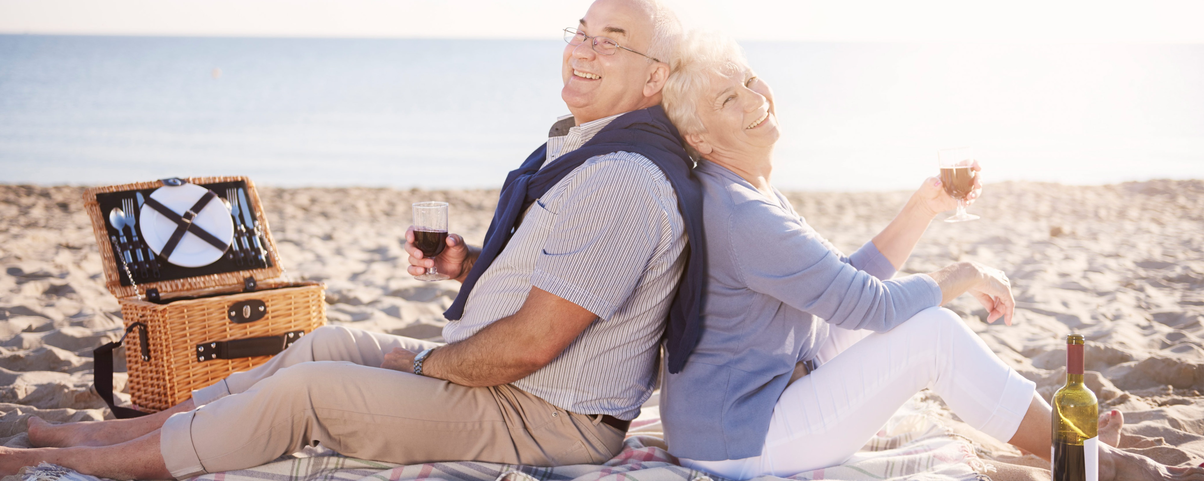 Älteres Paar sitzt am Strand mit Picknickkorb und Weinflasche, genießt entspannten Urlaub am Meer​​​​​​​​​​​​​​​​​​​​​​​​​​​​​​​​​​​​​​​​​​​​​​​​
