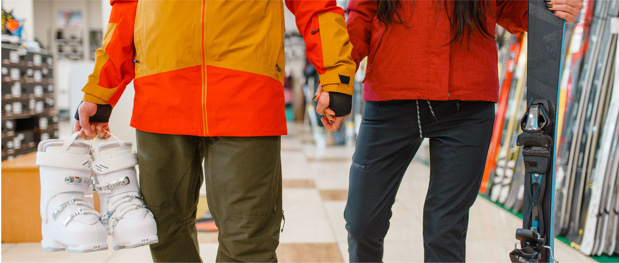 Paar in Winterjacken hält Skischuhe und Ski in einem Sportgeschäft mit Skiausrüstung im Hintergrund​​​​​​​​​​​​​​​​​​​​​​​​​​​​​​​​​​​​​​​​​​​​​​