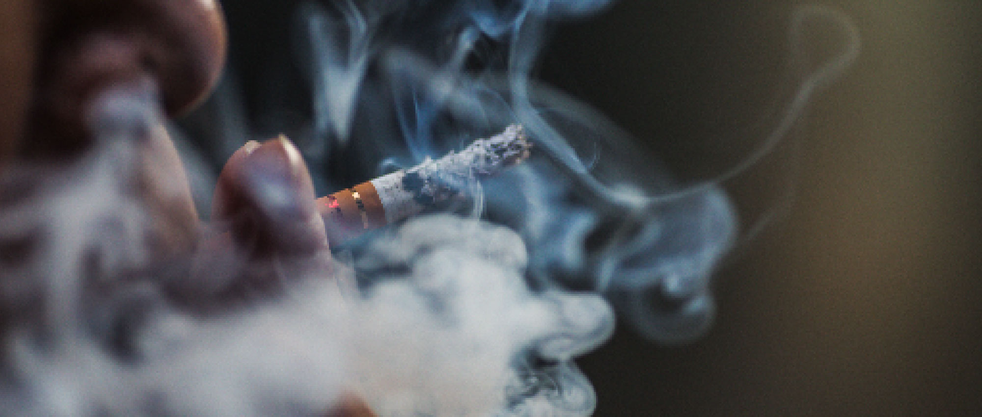 Nahaufnahme einer Person, die eine Zigarette raucht, umgeben von Rauch. Thema Rauchen und Hörminderung sichtbar.​​​​​​​​​​​​​​​​​​​​​​​​​​​​​​​​​