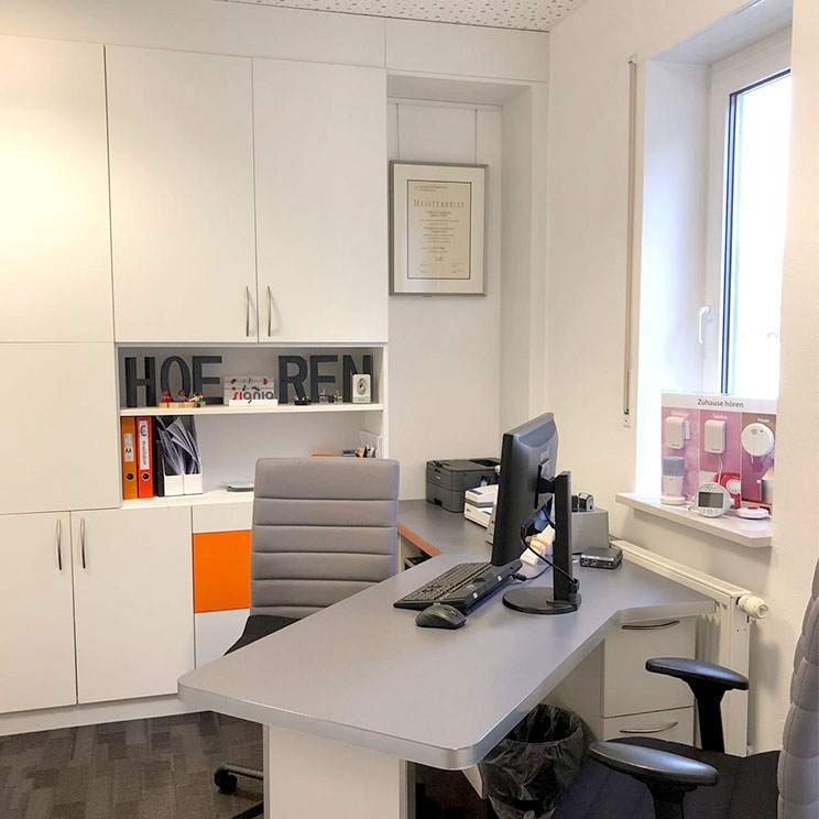 Helles Büro mit Schreibtisch, Computer, Akustikgeräten am Fenster und moderner Einrichtung für Hörakustiker​​​​​​​​​​​​​​​​​​​​​​​​​​​​​​​​​​​​​​