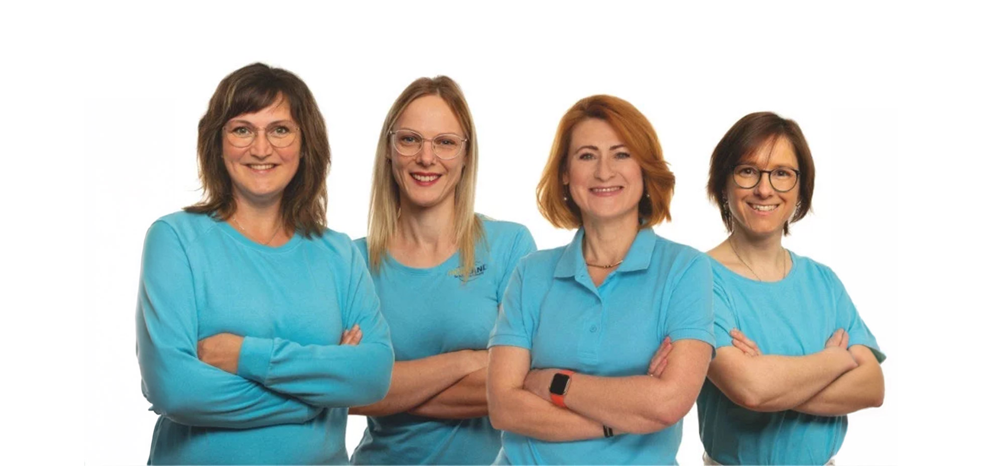 Vier Frauen in blauen Oberteilen stehen mit verschränkten Armen vor weißem Hintergrund und lächeln freundlich​​​​​​​​​​​​​​​​​​​​​​​​​​​​​​​​​​​​