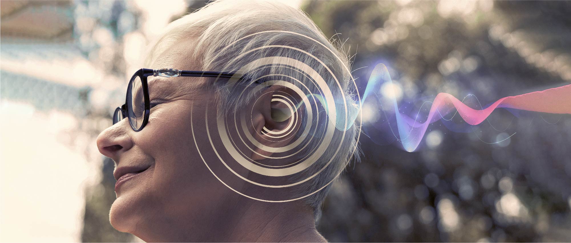 Ältere Frau mit Brille trägt modernes Hörgerät, umgeben von digitaler Klangwelle, draußen bei Tageslicht​​​​​​​​​​​​​​​​​​​​​​​​​​​​​​​​​​​​​​​​​