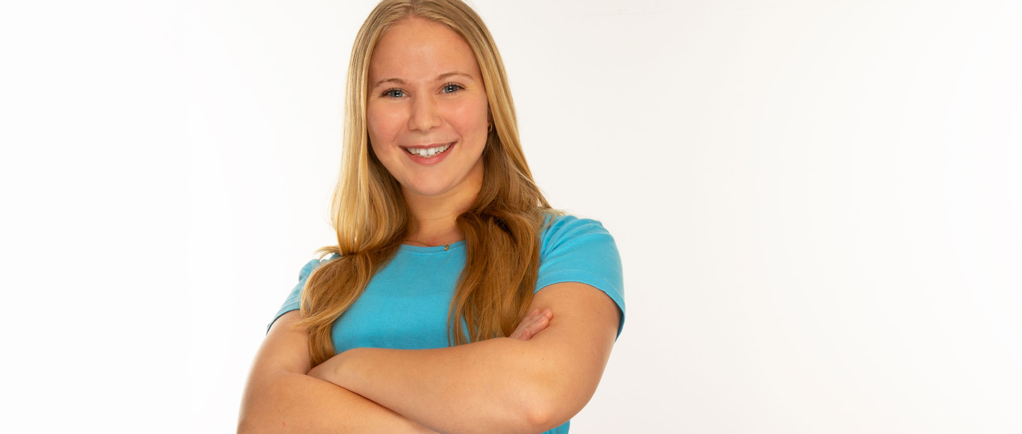 Porträt einer jungen Frau mit langen blonden Haaren und blauem Shirt vor hellem Hintergrund, freundlich und selbstbewusst​​​​​​​​​​​​​​​​​​​​​​​​