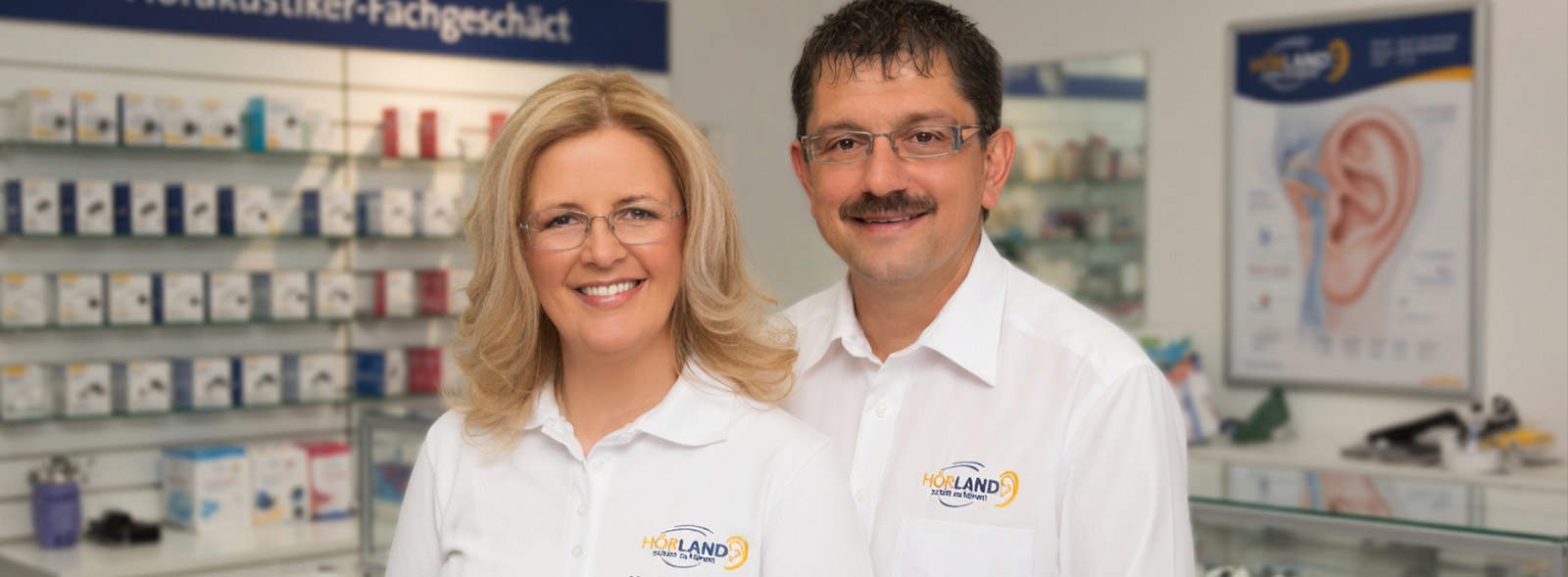 Zwei Hörakustiker im Fachgeschäft vor Regalen mit Hörgeräten und Zubehör in freundlicher Atmosphäre​​​​​​​​​​​​​​​​​​​​​​​​​​​​​​​​​​​​​​​​​​​​​​