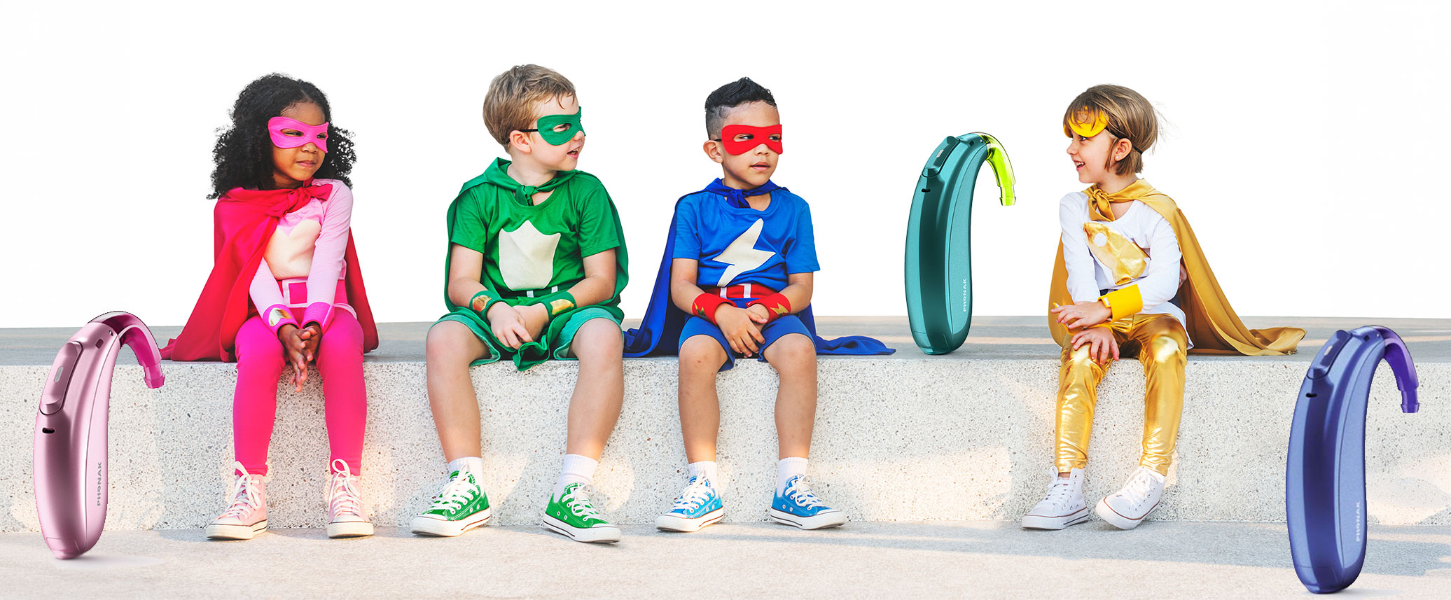 Vier Kinder in farbenfrohen Superheldenkostümen sitzen nebeneinander mit bunten Hörgeräten auf weißem Hintergrund​​​​​​​​​​​​​​​​​​​​​​​​​​​​​​​​