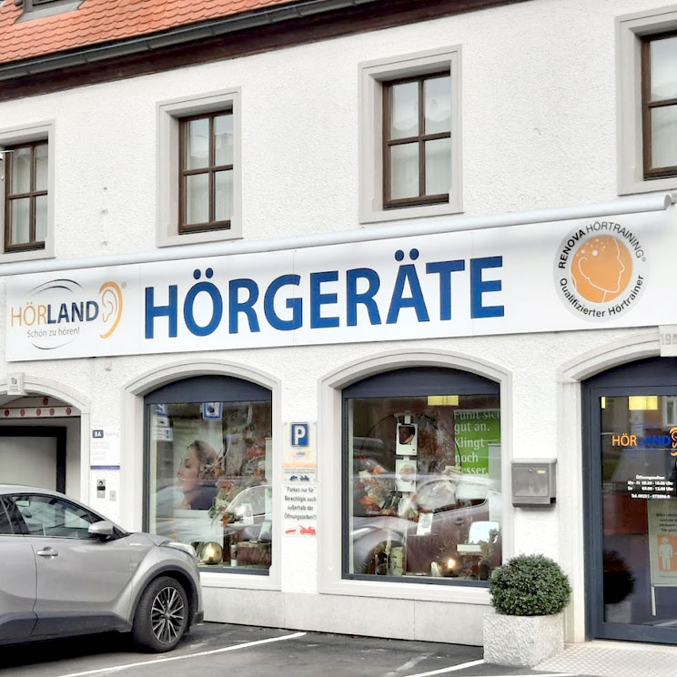 Außenansicht des Hörland Hörgerätegeschäfts in Marktredwitz mit Schaufenstern, Parkplätzen und Firmenlogo.​​​​​​​​​​​​​​​​​​​​​​​​​​​​​​​​​​​​​​​