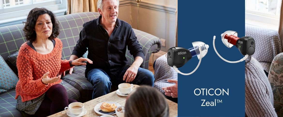 Drei Menschen sitzen im Wohnzimmer und unterhalten sich entspannt. Oticon Zeal Hörgeräte sind eingeblendet.​​​​​​​​​​​​​​​​​​​​​​​​​​​​​​​​​​​​​​