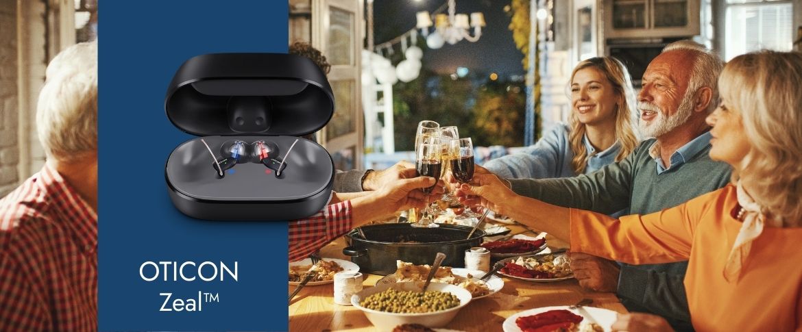 Oticon Zeal Hörgeräte im Ladeetui neben einer Gruppe, die beim Abendessen anstößt. Gemütliche Stimmung und gemeinsames Essen.​​​​​​​​​​​​​​​​​​​​