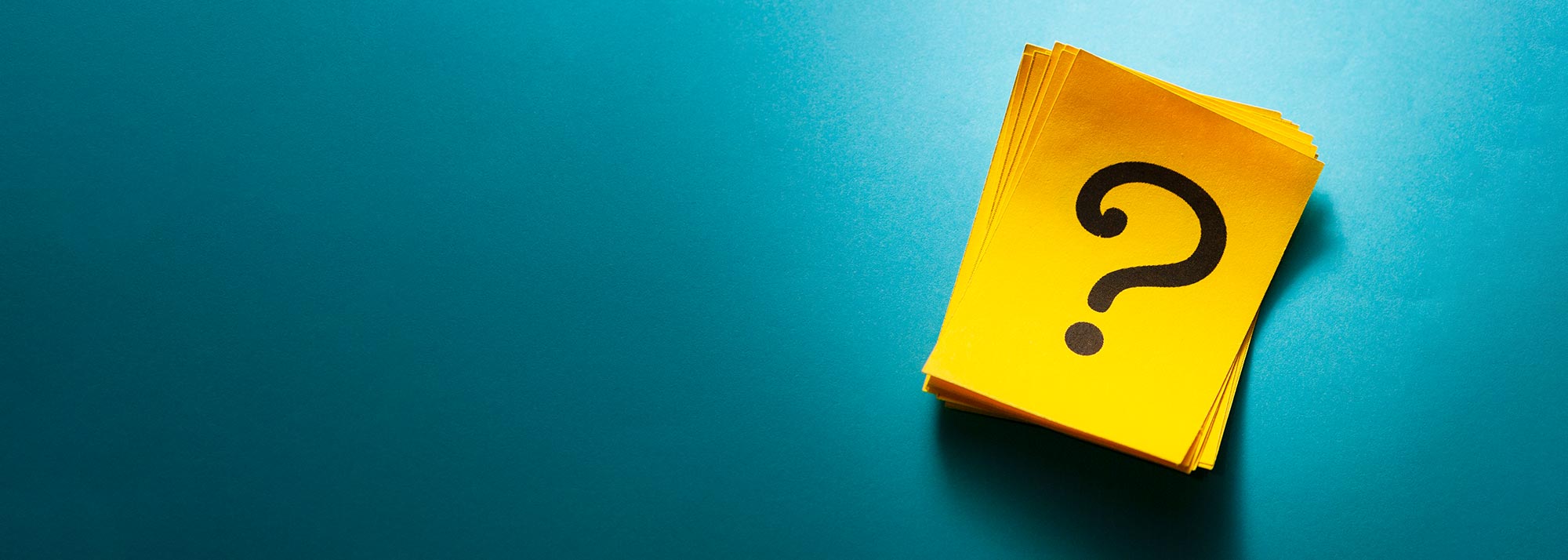 Ein Stapel gelber Karten mit schwarzem Fragezeichen liegt auf blauem Untergrund, symbolisiert Unsicherheit und Fragen.​​​​​​​​​​​​​​​​​​​​​​​​​​​