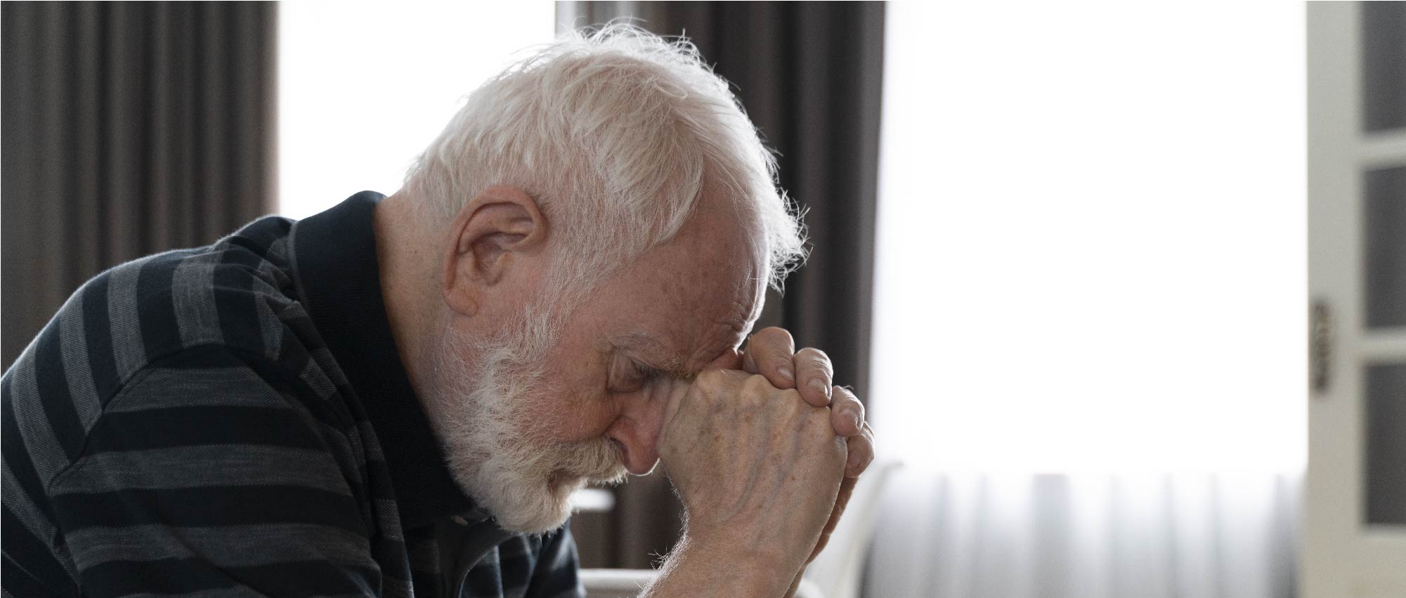 Porträt eines älteren Mannes mit weißem Haar und Bart, der nachdenklich die Hände hält, symbolisiert Hörgeräteversorgung.​​​​​​​​​​​​​​​​​​​​​​​​