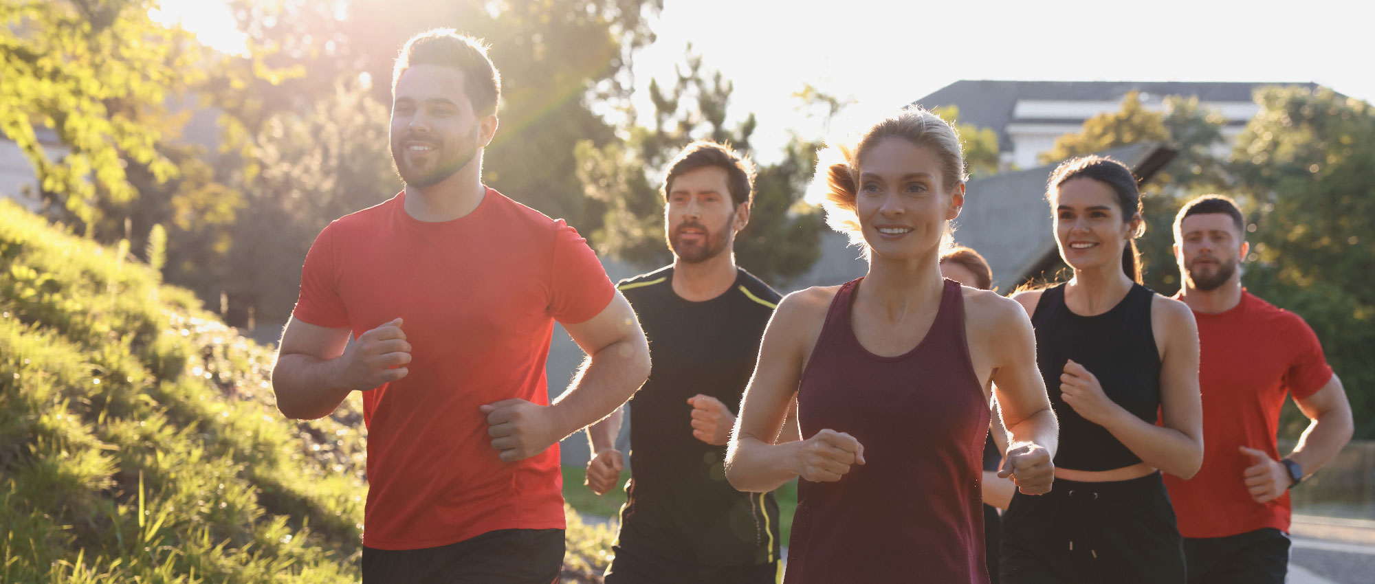 Fünf Personen joggen gemeinsam im Park bei Sonnenlicht, umgeben von Bäumen und grüner Natur, sportliche Stimmung​​​​​​​​​​​​​​​​​​​​​​​​​​​​​​​​​