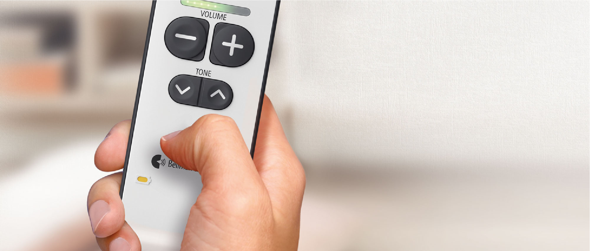 Nahaufnahme einer Hand, die eine Fernbedienung mit Lautstärke- und Toneinstellungen in hellem Raum hält​​​​​​​​​​​​​​​​​​​​​​​​​​​​​​​​​​​​​​​​​​