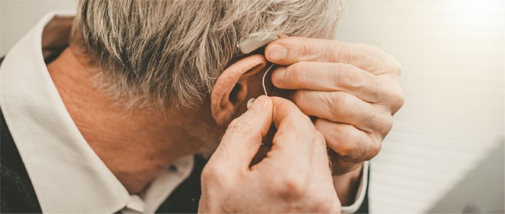Älterer Mann steckt ein veraltetes Hörsystem ins Ohr, Nahaufnahme mit Fokus auf Hände und graues Haar​​​​​​​​​​​​​​​​​​​​​​​​​​​​​​​​​​​​​​​​​​​​