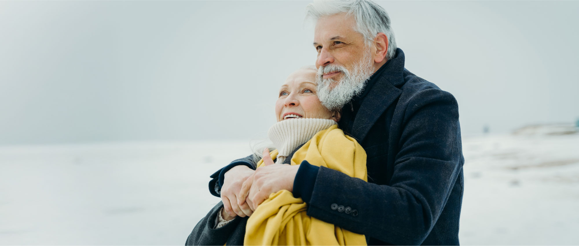 Älteres Paar in Winterkleidung umarmt sich draußen in verschneiter Landschaft bei kalter Witterung​​​​​​​​​​​​​​​​​​​​​​​​​​​​​​​​​​​​​​​​​​​​​​​